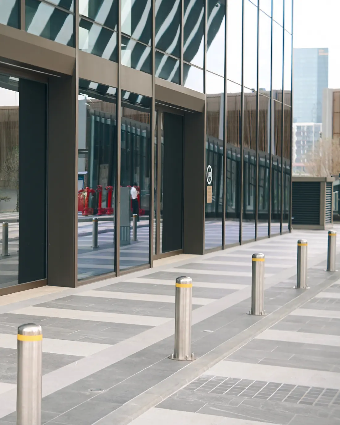 A row of stainless steel bollards with yellow bands protecting the glass frontage of a commercial building